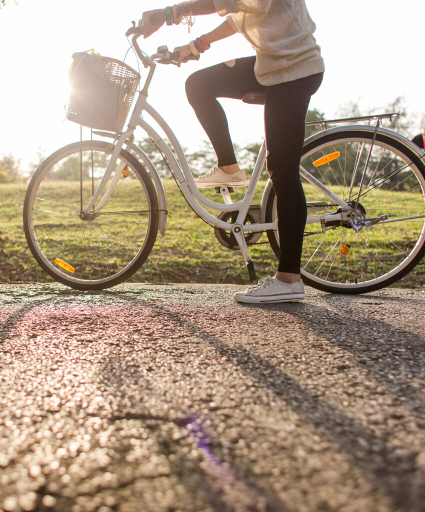 A young woman is about to ride a bike in a sunny park. The bicycle has a basket.